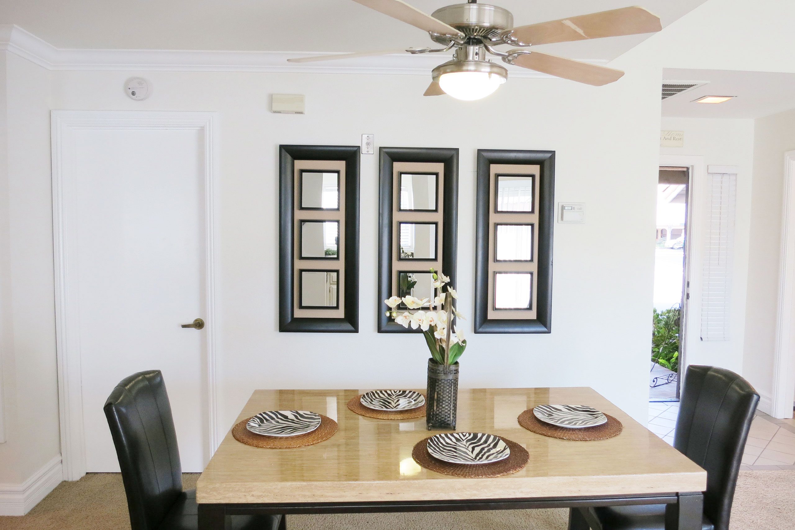 Two Bedroom Apartments in Anaheim CA - Le Med - Dining Room with a Dining Table with Plates, Flowers, a Ceiling Fan, and Plush Carpet